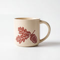 ROOT24STUDIO The Acorn Mug featuring raised terracotta oak leaves and acorn relief on speckled vanilla ceramic