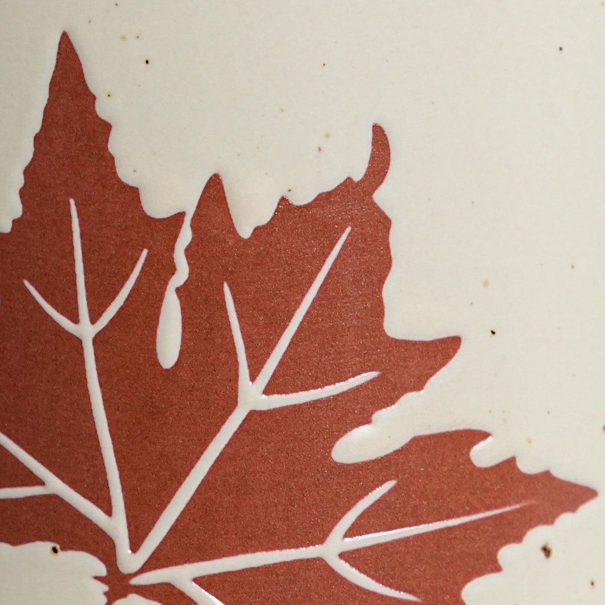 Macro detail of tactile wax-resist maple leaf relief on matte speckled Vanilla Ice glaze