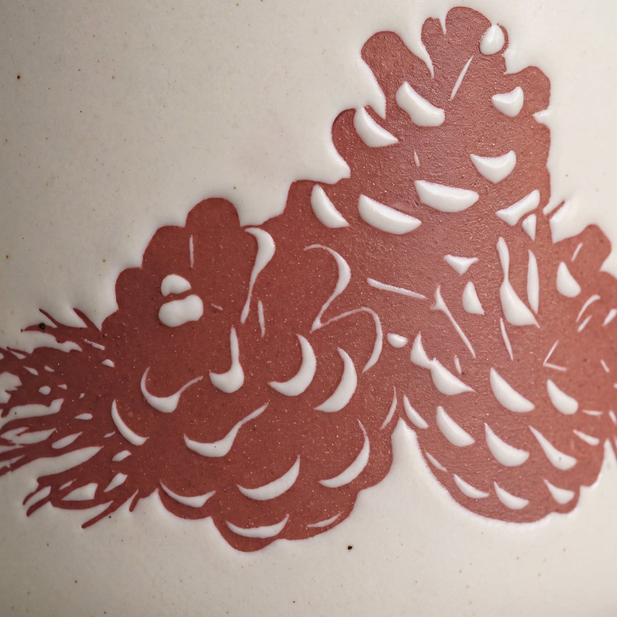 Macro detail of handcrafted three-pinecone raised relief motif showing natural glaze texture