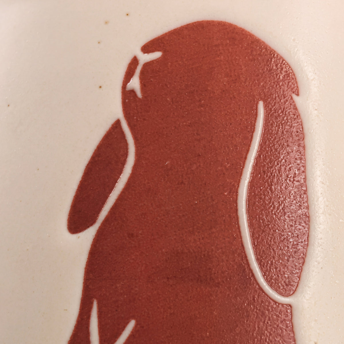 Macro detail of tactile wax-resist standing lop bunny relief on matte speckled Vanilla Ice glaze