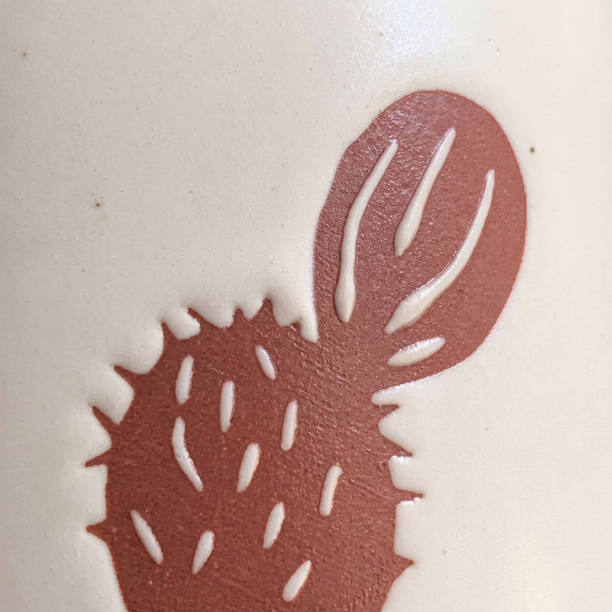 Close-up of the raised prickly pear sprout motif showing fine tactile spines and natural clay speckles