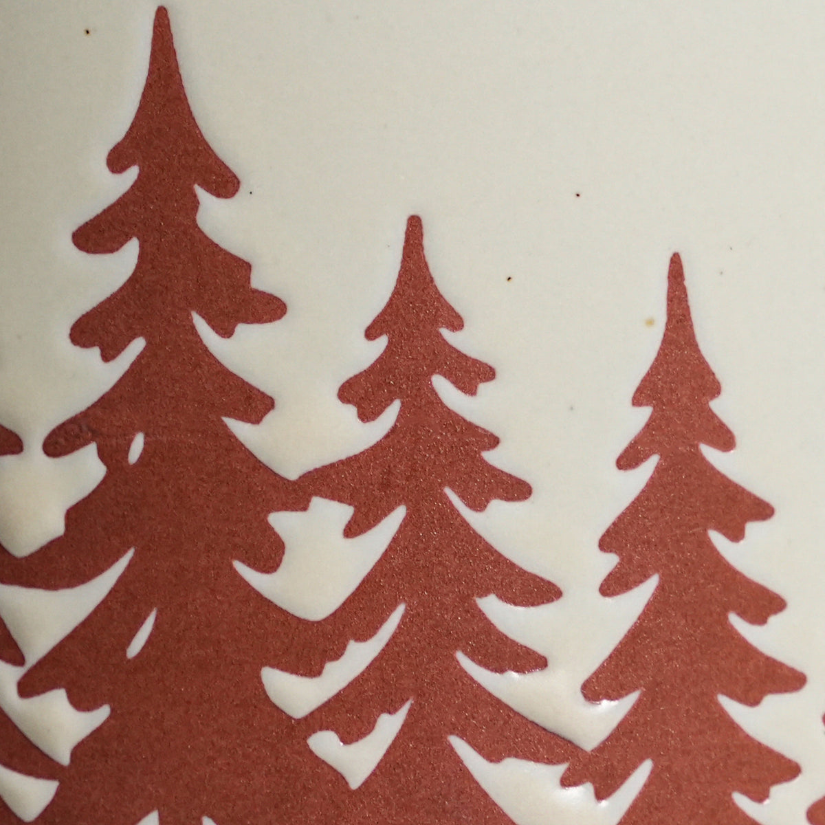 Macro detail of tactile wax-resist pine tree crown relief on speckled Vanilla Ice glaze