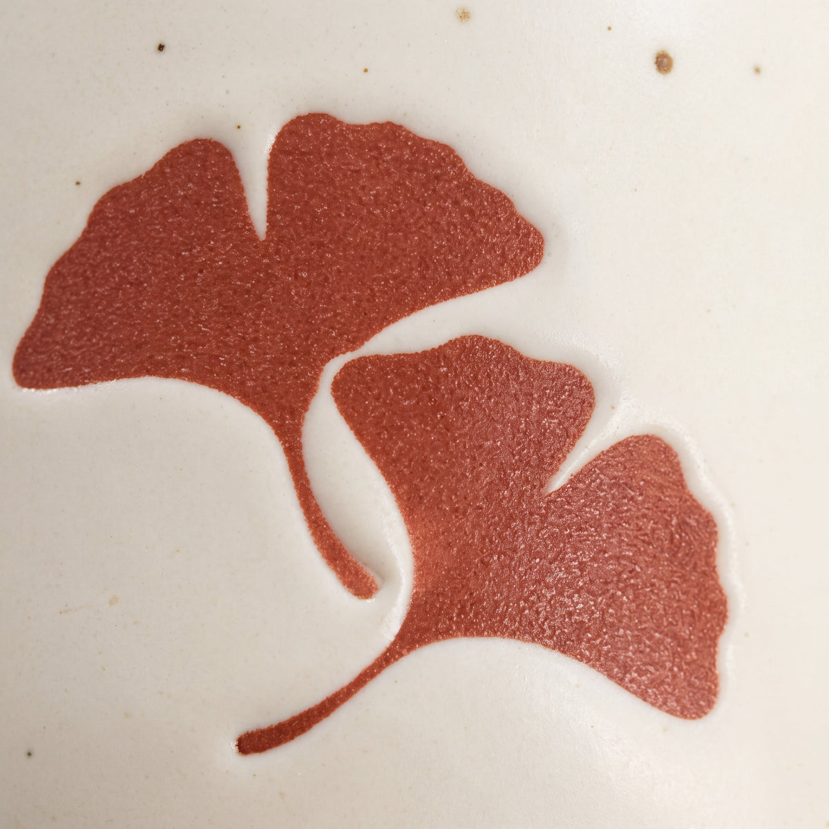 Close-up of tactile wax-resist twin ginkgo leaf relief on matte speckled Vanilla Ice glaze