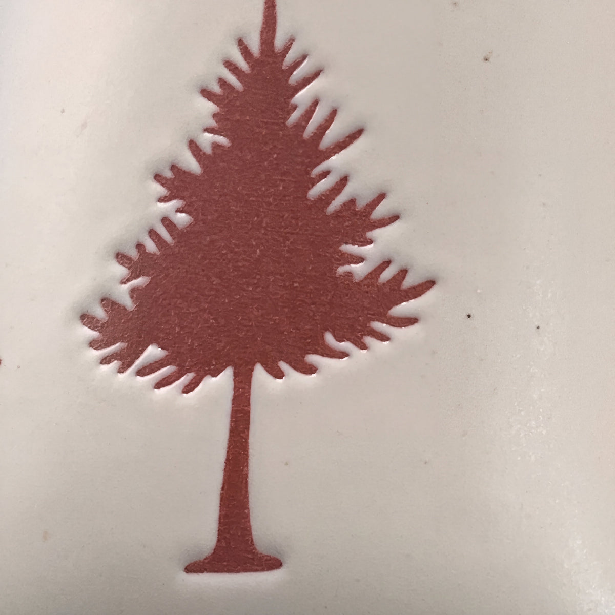 Close-up of tactile wax-resist pine tree relief on matte speckled stoneware ceramic