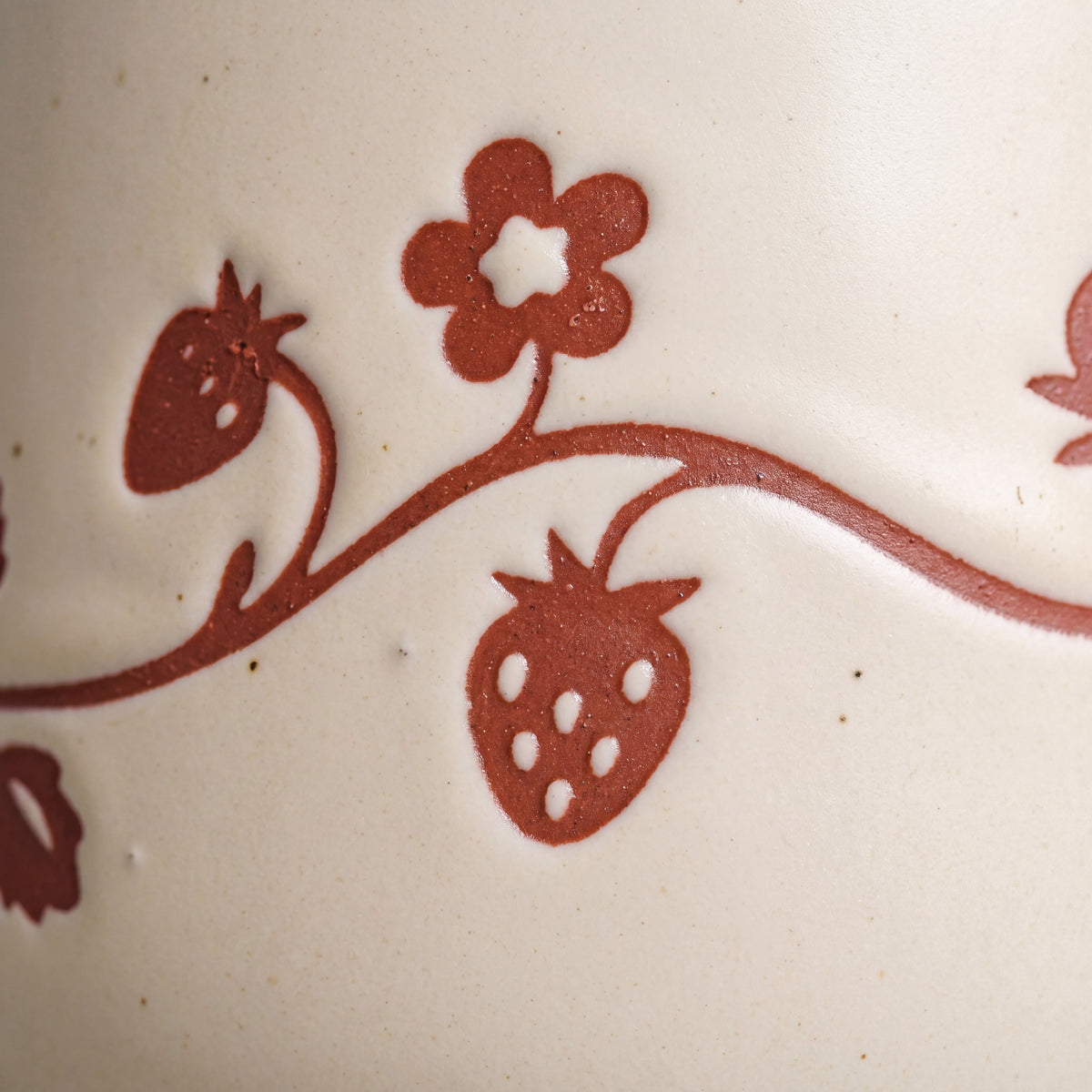 Macro detail of tactile wax-resist wild strawberry fruit and blossom relief on matte speckled glaze