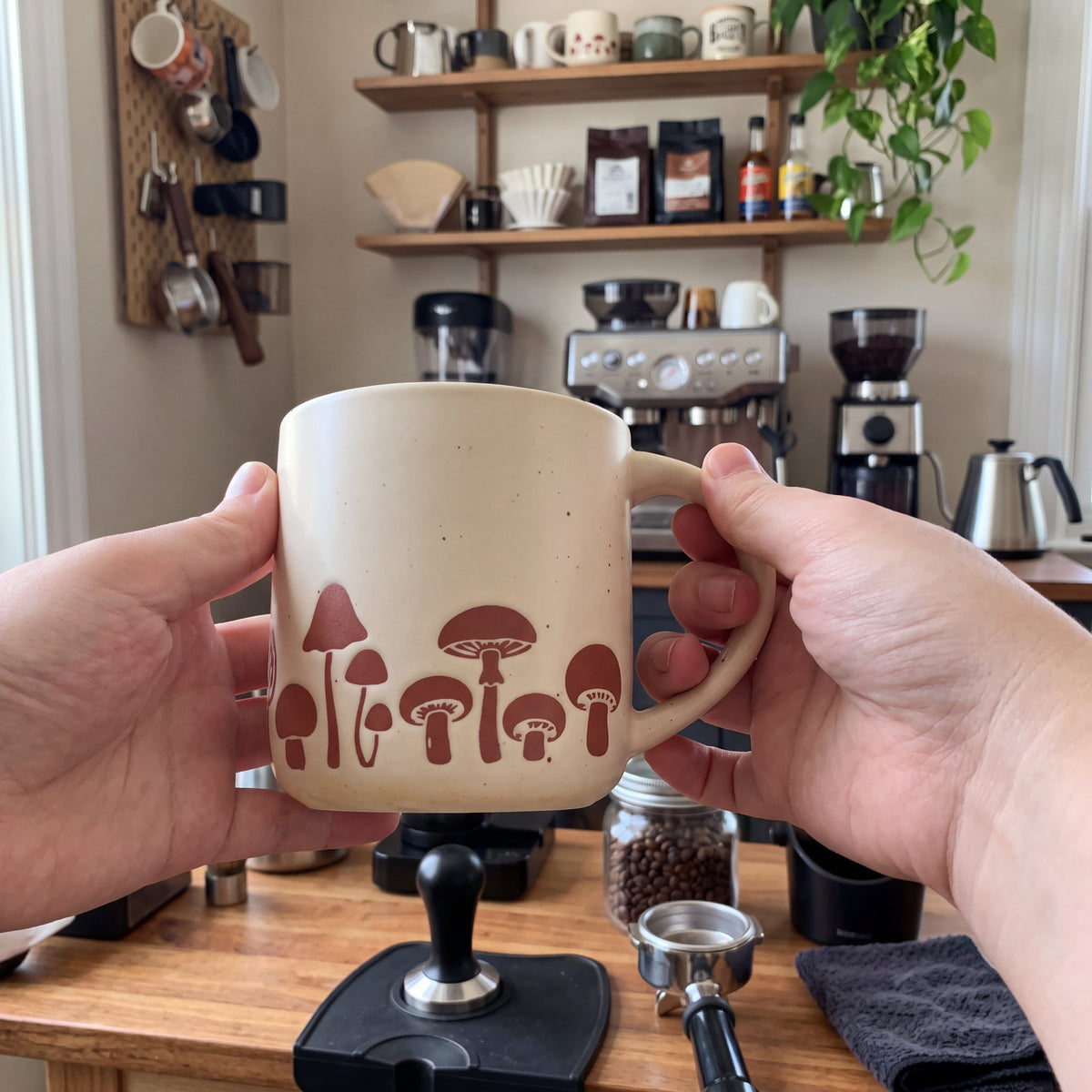 Two hands cradling The Mushroom ceramic mug at a cozy home coffee bar station