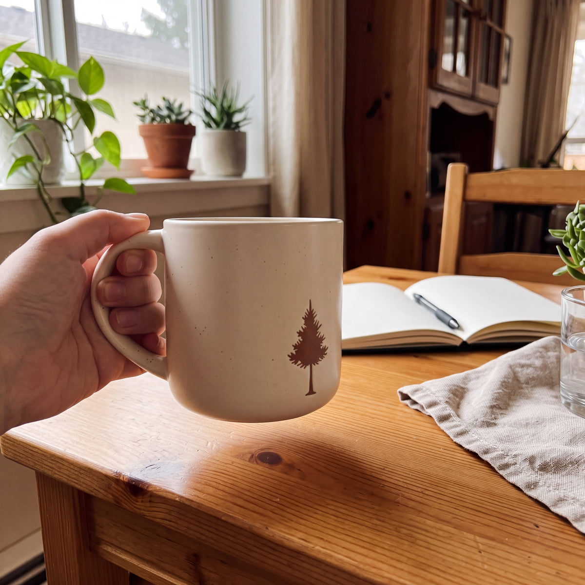Aesthetic morning coffee ritual with stoneware pinecone mug held over a sunlit wooden desk with journal and linen
