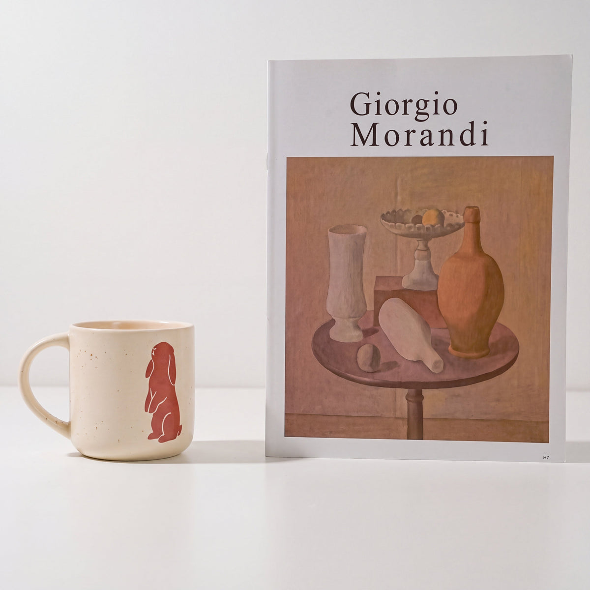 Minimalist styling of The Bunny stoneware mug showing standing rabbit motif beside Morandi art book