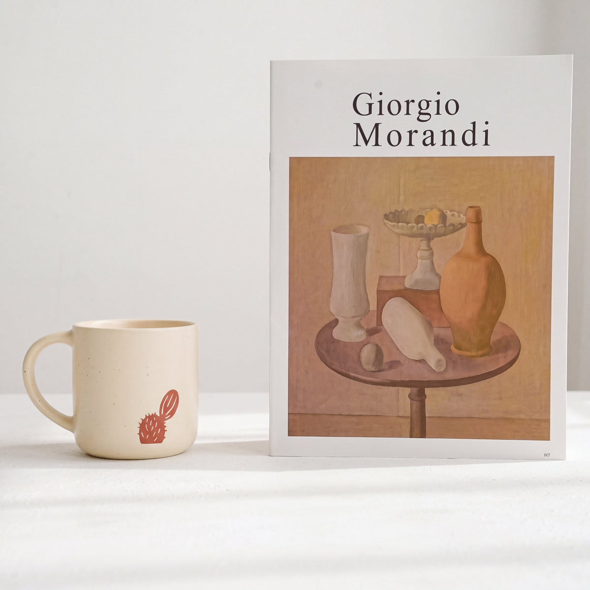 Minimalist styling of The Cactus stoneware mug showing prickly pear motif beside Morandi art book