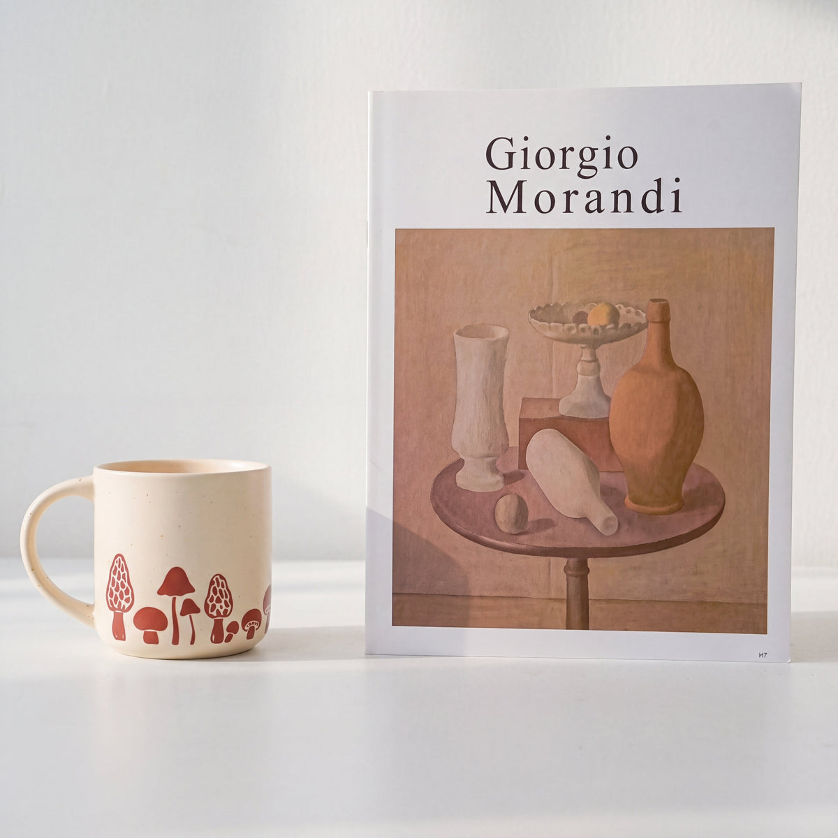 Minimalist styling of The Mushroom stoneware mug next to a Giorgio Morandi art book