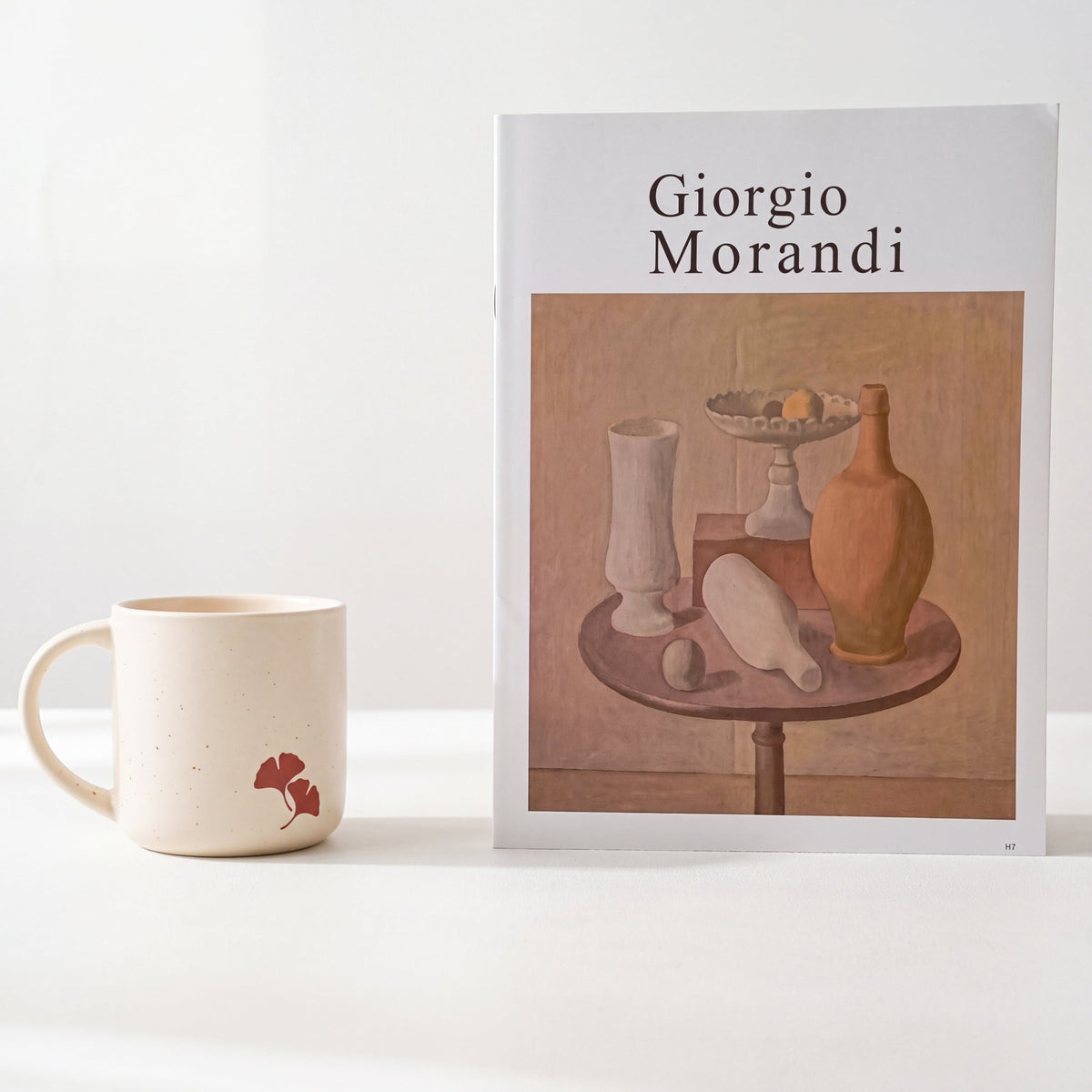 Minimalist styling of The Ginkgo stoneware mug showing twin leaf motif beside Morandi art book