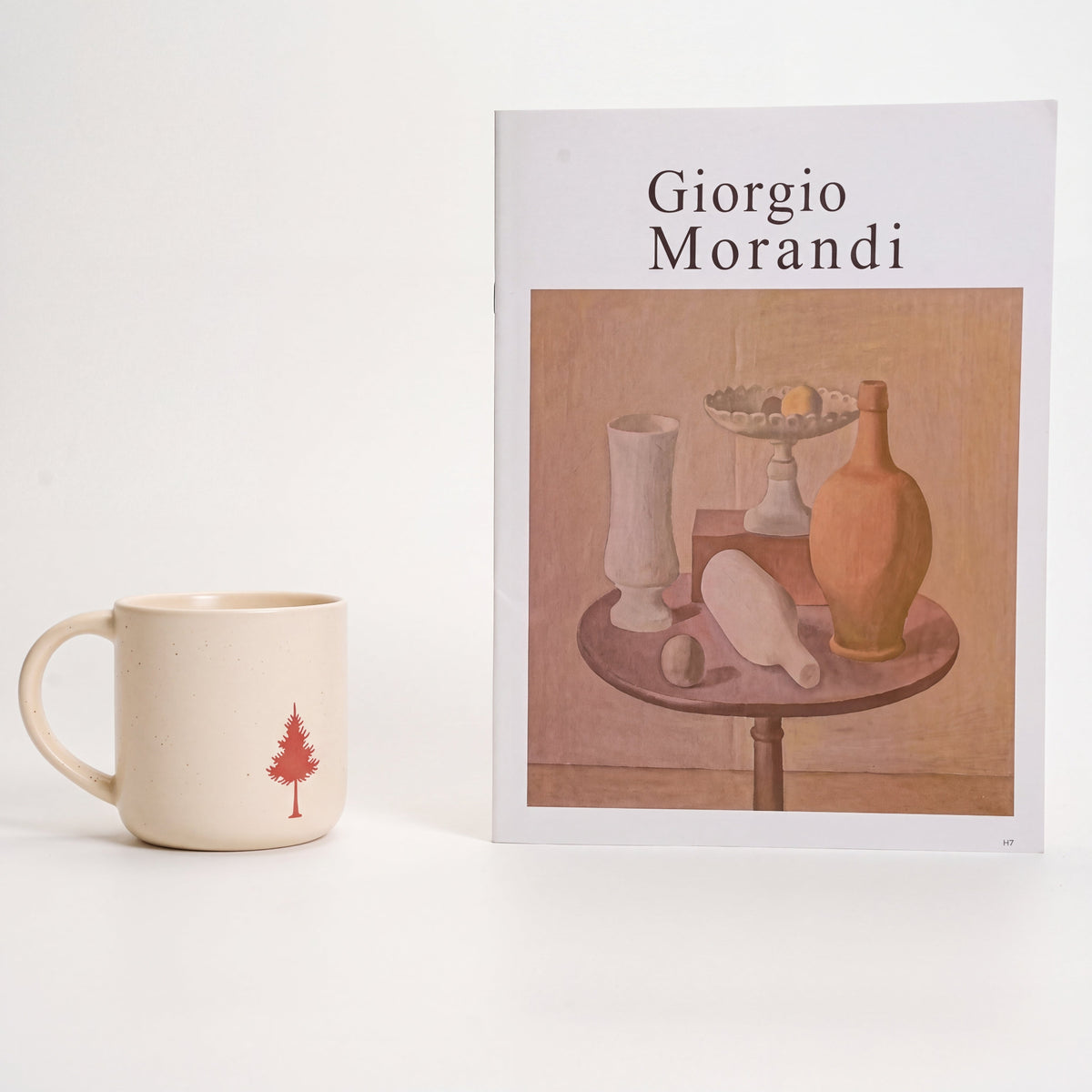 Handcrafted ceramic mug with pine tree relief motif styled beside a Morandi art book