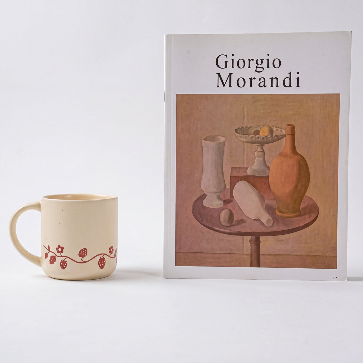 Minimalist styling of The Wild Strawberry stoneware mug showing vine motif beside Morandi art book