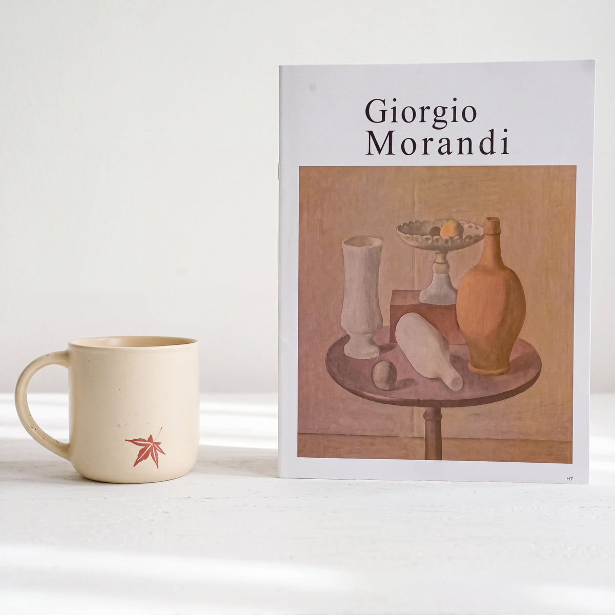 Minimalist styling of The Maple stoneware mug showing solitary leaf motif beside Morandi art book